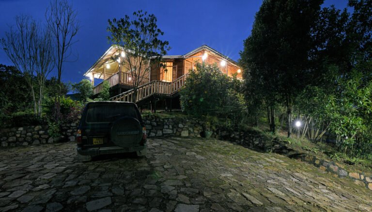 A vehicle parked on a stone driveway outside a lit lodge at dusk